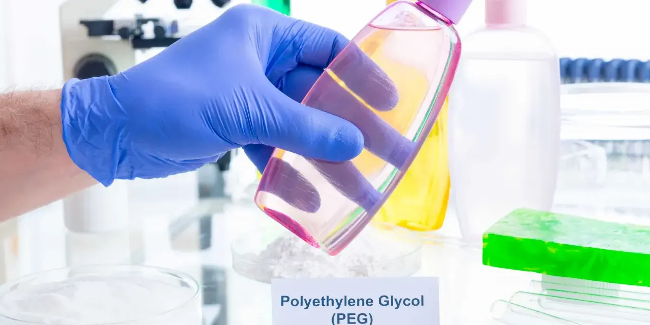 Ręka w niebieskiej rękawiczce trzyma buteleczkę z różowym płynem, w tle laboratorium i kosmetyki.