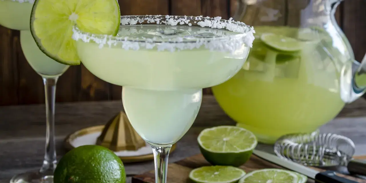 Spicy Margarita przepis: orzeźwiający drink z solą na brzegu kieliszka, limonkami i dzbankiem pełnym zielonego napoju.