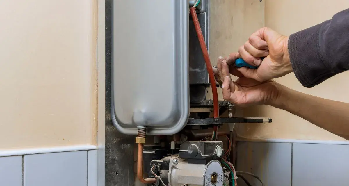 Mani che riparano uno scaldabagno a gas: il bruciatore non parte. Si vede il tecnico con un cacciavite blu.