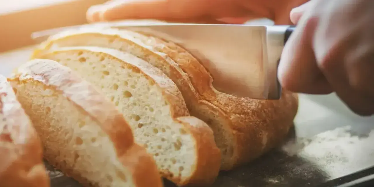 Ręce kroją świeży chleb na kromki. Dowiedz się, jak odświeżyć chleb, by był jak nowy.