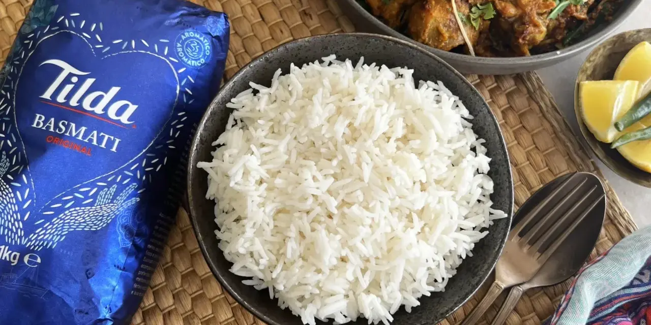 Un tazón de arroz basmati blanco y esponjoso junto a un paquete de Tilda Basmati Original.