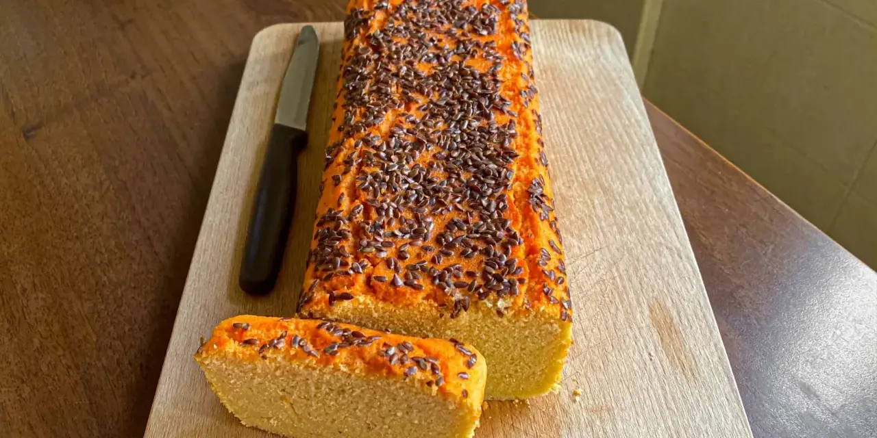 Pane di lenticchie con semi di lino, affettato su tagliere di legno, accanto a un coltello.