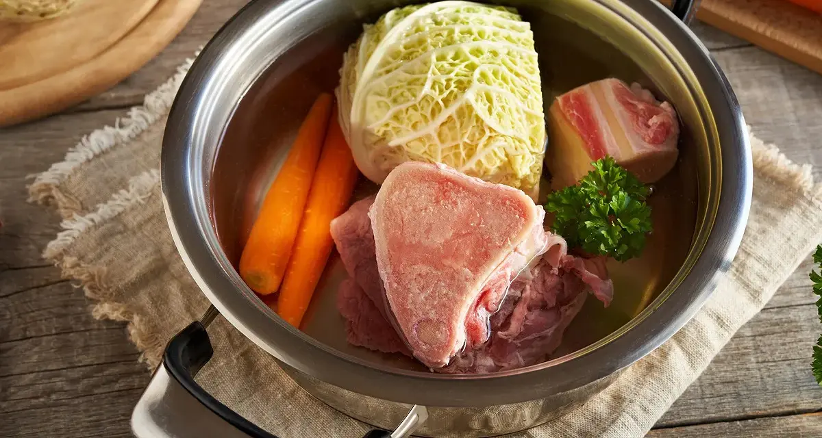 Une marmite remplie d'ingrédients pour une potee au chou : chou, carottes, viande et os.