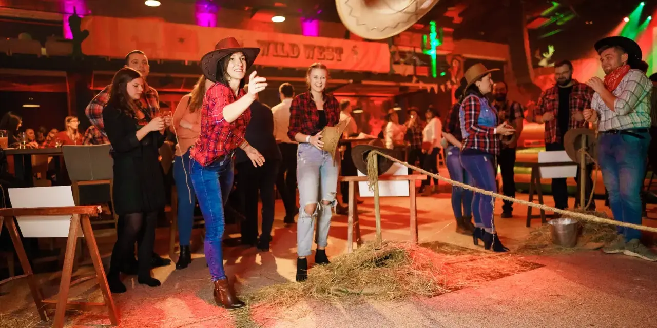 Impreza w stylu country: kobiety w kratkach i kapeluszach rzucają kapeluszem do celu.