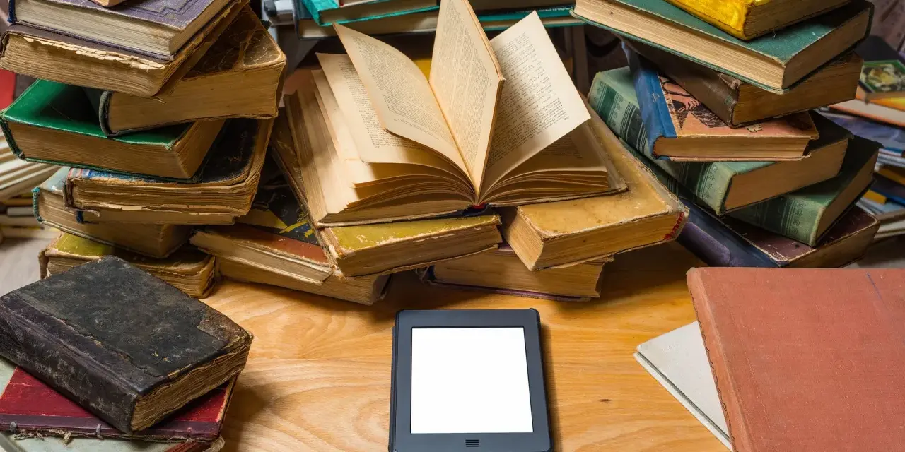Stosy starych książek i nowoczesny ebook na drewnianym blacie. Wybór między tradycją a technologią.