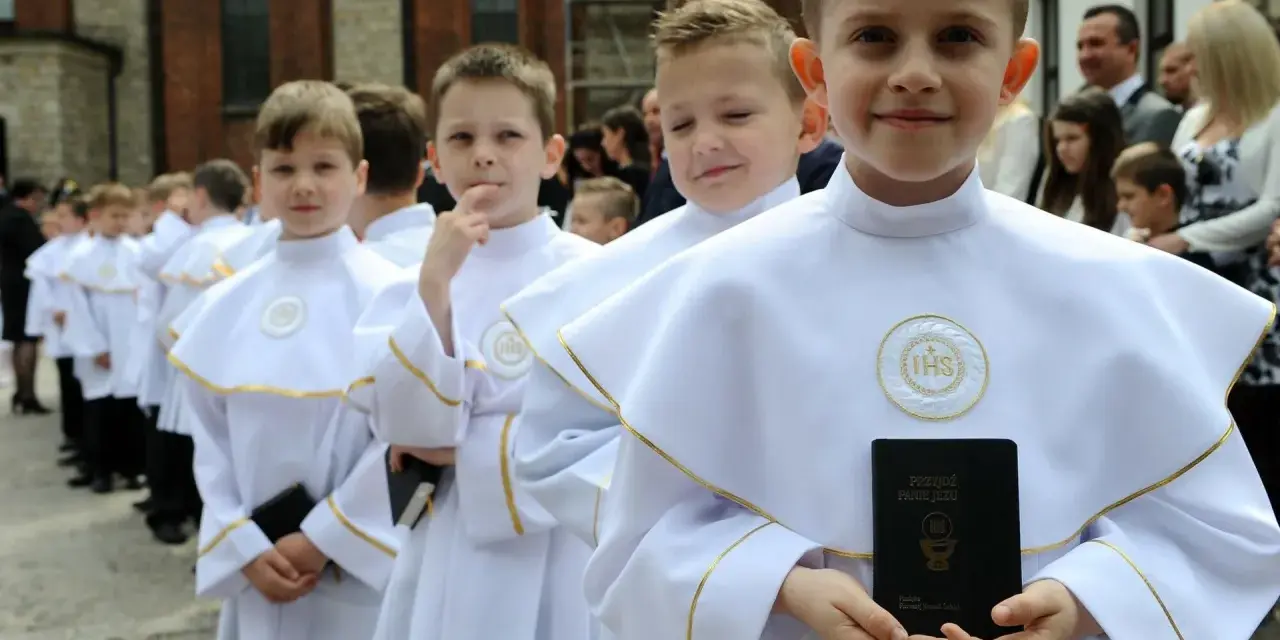 Chłopcy w białych albach, gotowi do komunii, trzymają modlitewniki. Jeden z nich uśmiecha się do aparatu.