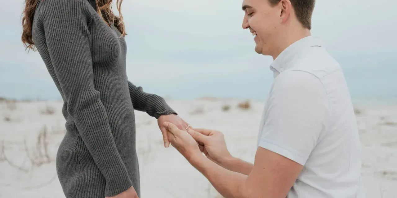 Mann macht Heiratsantrag am Strand. Ab wann darf man sich verloben? Das ist eine Frage der Liebe, nicht des Alters.