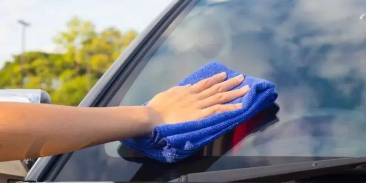 Mano con paño azul limpiando los cristales del coche para una visibilidad perfecta.