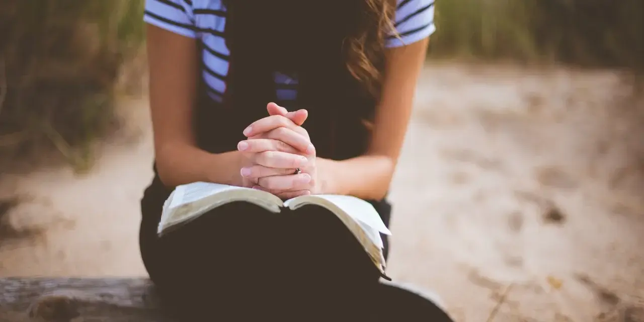 Frau mit verschränkten Händen über einem offenen Buch, die über ihre fertigen Gebete nachdenkt.