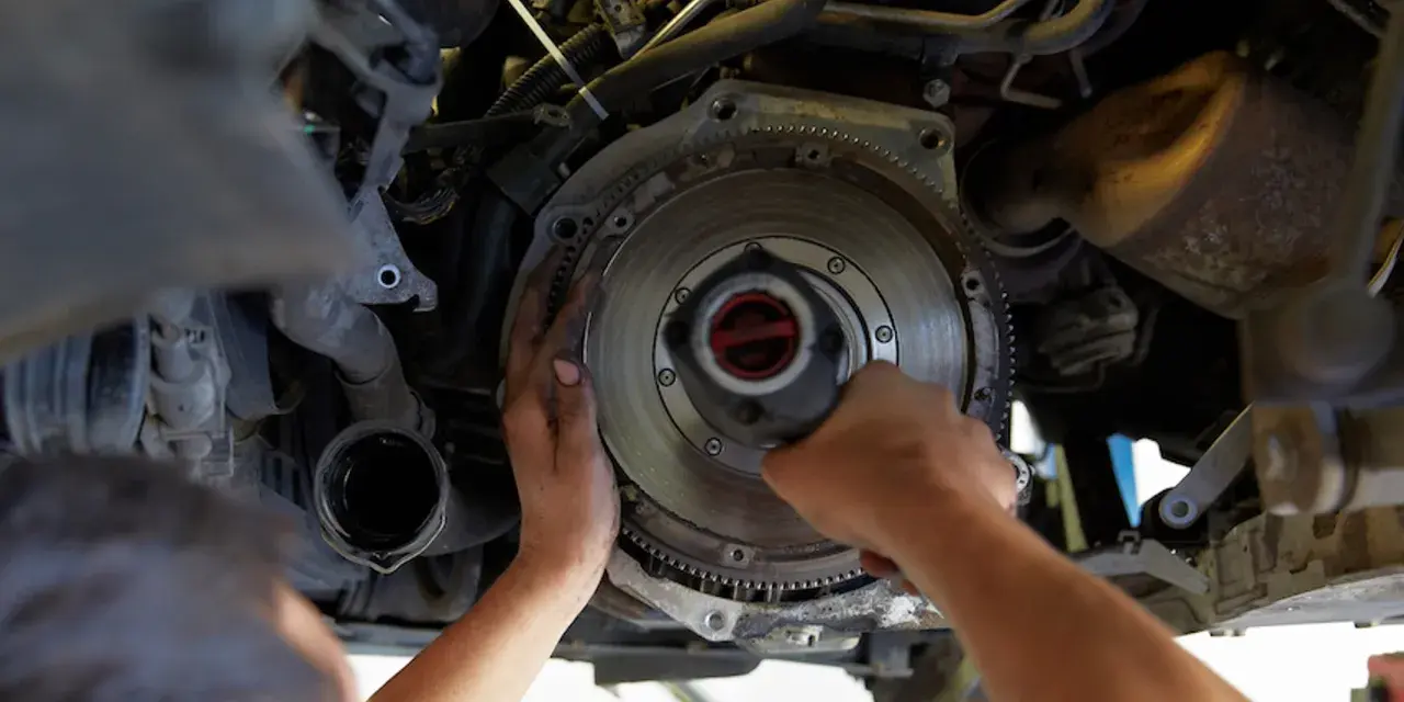 Mechanik dokonuje wymiany dwumasy w samochodzie, pracując przy skrzyni biegów.
