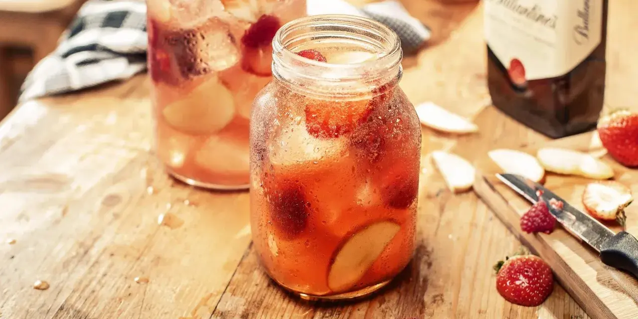 Orzeźwiający, kobiecy drink z whisky, pełen truskawek i jabłek, na drewnianym blacie.