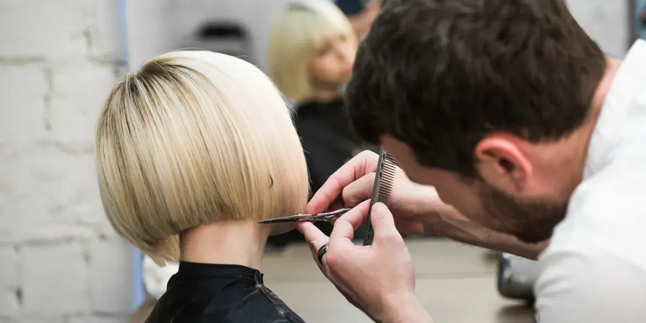 Fryzjerka tworzy modne fryzury odmładzające po 40 krótkie. Blond bob jest precyzyjnie cięty.