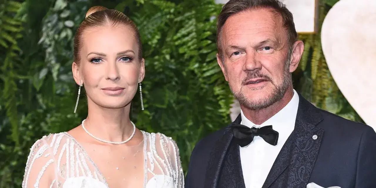 Cezary Pazura z żoną Edytą na ściance. Ona w białej, zdobionej sukni, on w eleganckim garniturze.