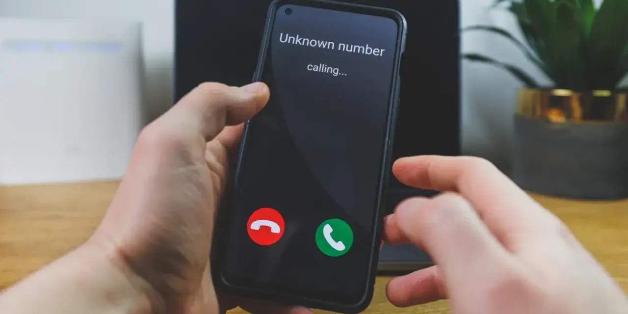 Dłoń trzyma telefon, na ekranie którego widnieje komunikat "Unknown number calling...". Czy odbierze, gdy numer prywatny dzwoni?