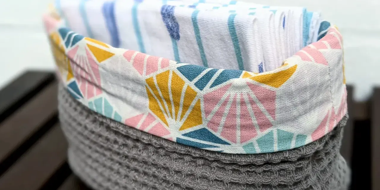 Un panier en tissu gris avec un motif géométrique coloré contient des mouchoirs en tissu. Une idée pour savoir que faire avec des mouchoirs en tissu.