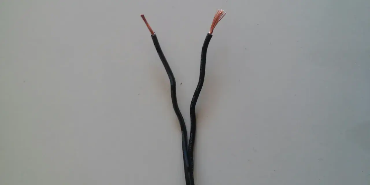 Dwa czarne przewody elektryczne rozchodzą się, odsłaniając miedziane końcówki. Czy czerwony to plus czy minus?