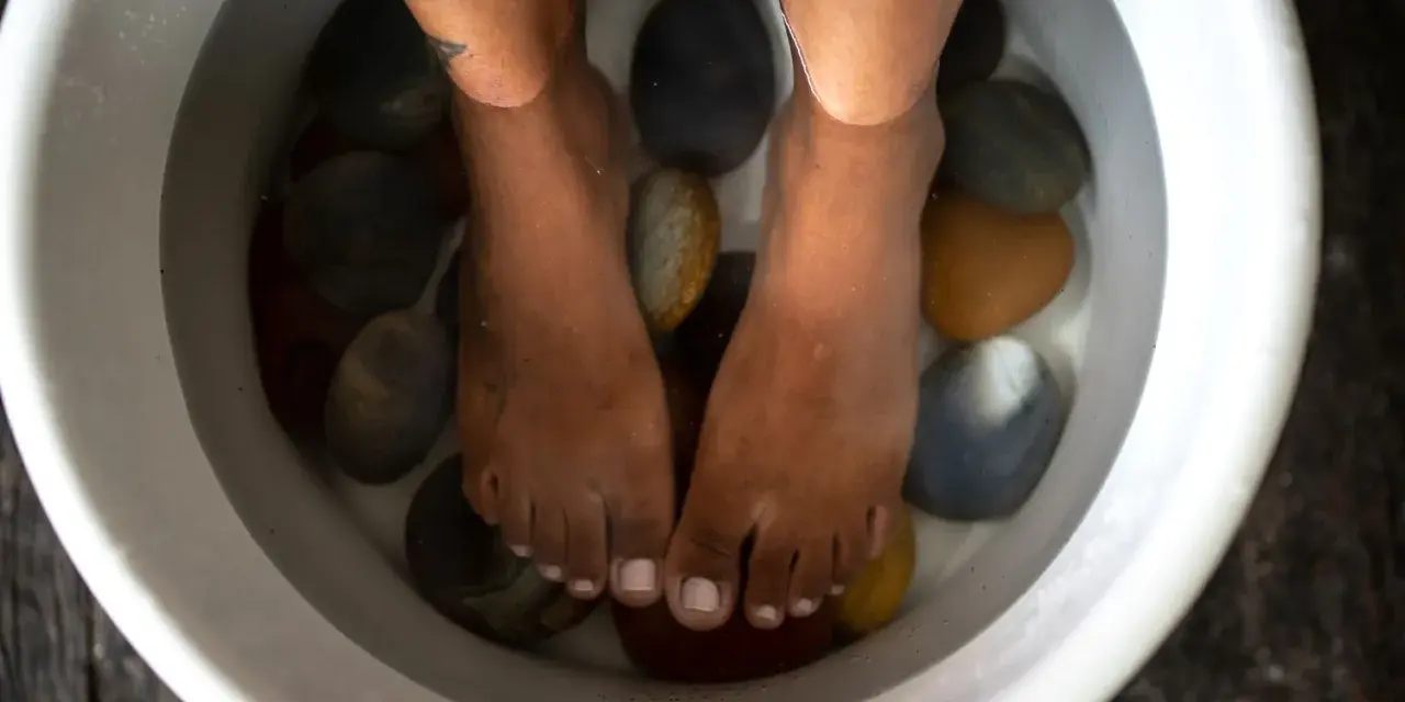 Feet submerged in a white basin filled with water and smooth stones, enjoying a relaxing salt water foot soak.