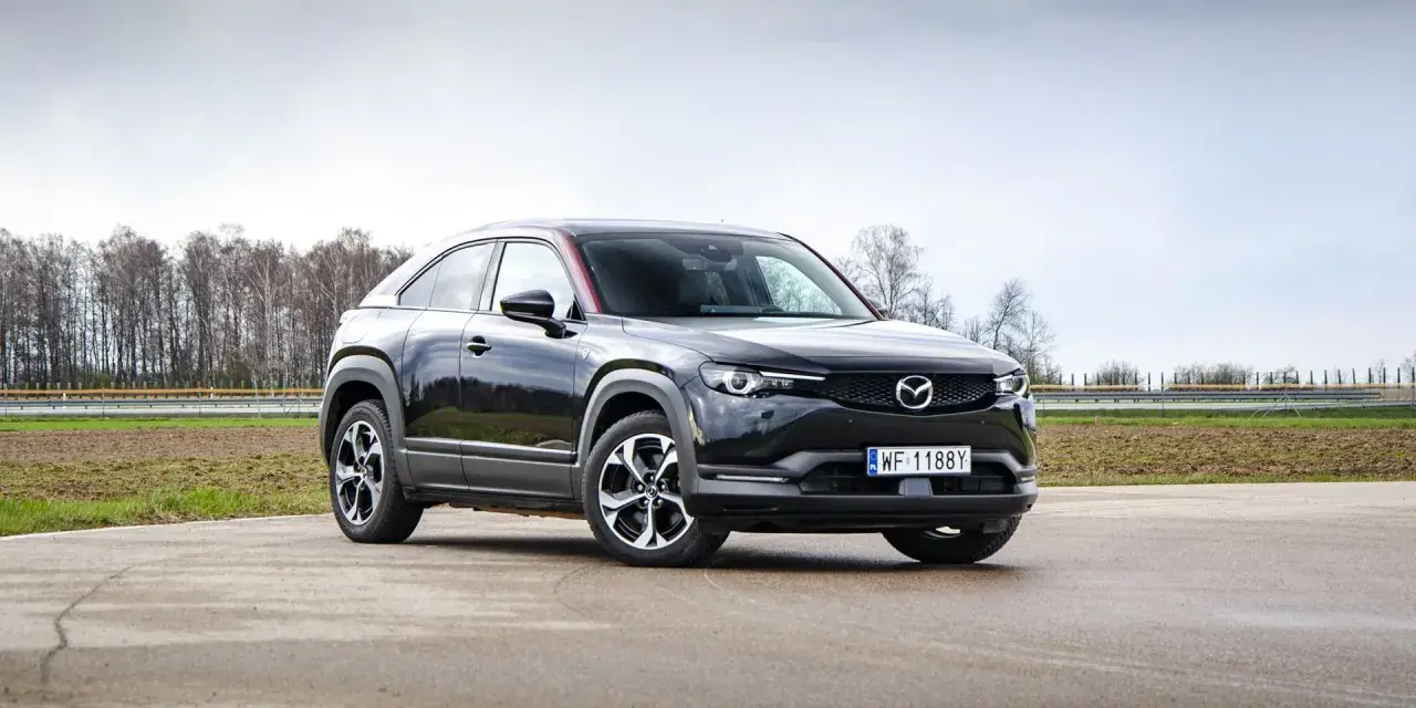 Czarna Mazda MX-30 na tle pochmurnego nieba i drzew.