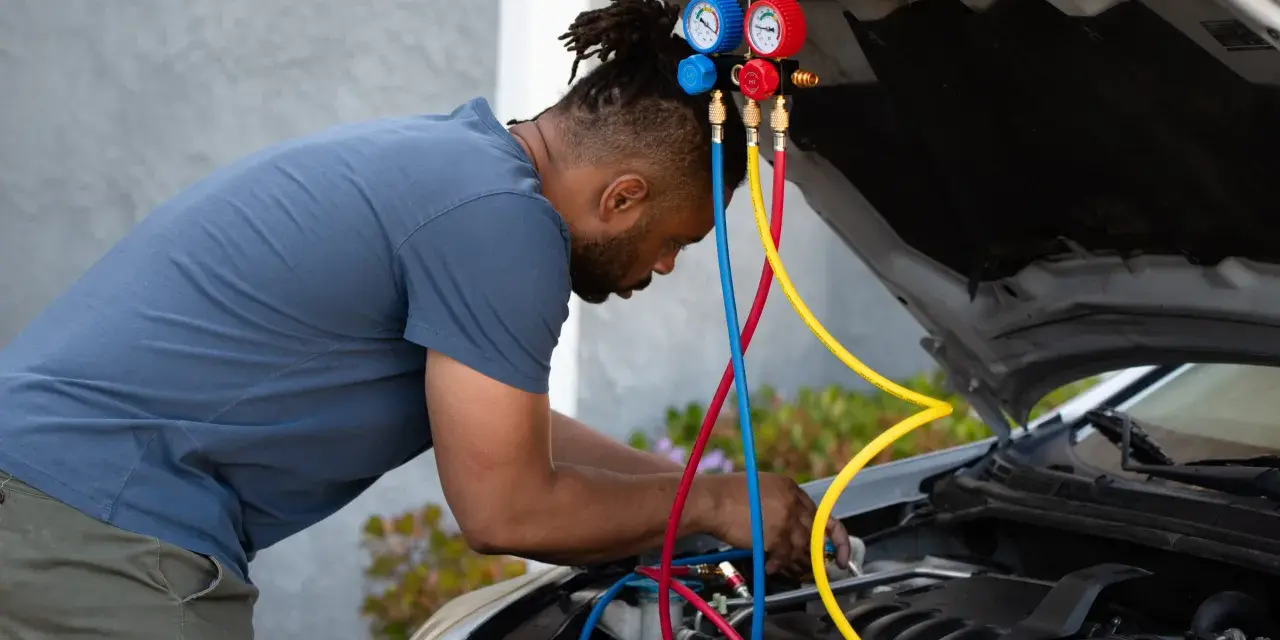 Man working on car engine, using gauges and hoses to fix car AC.