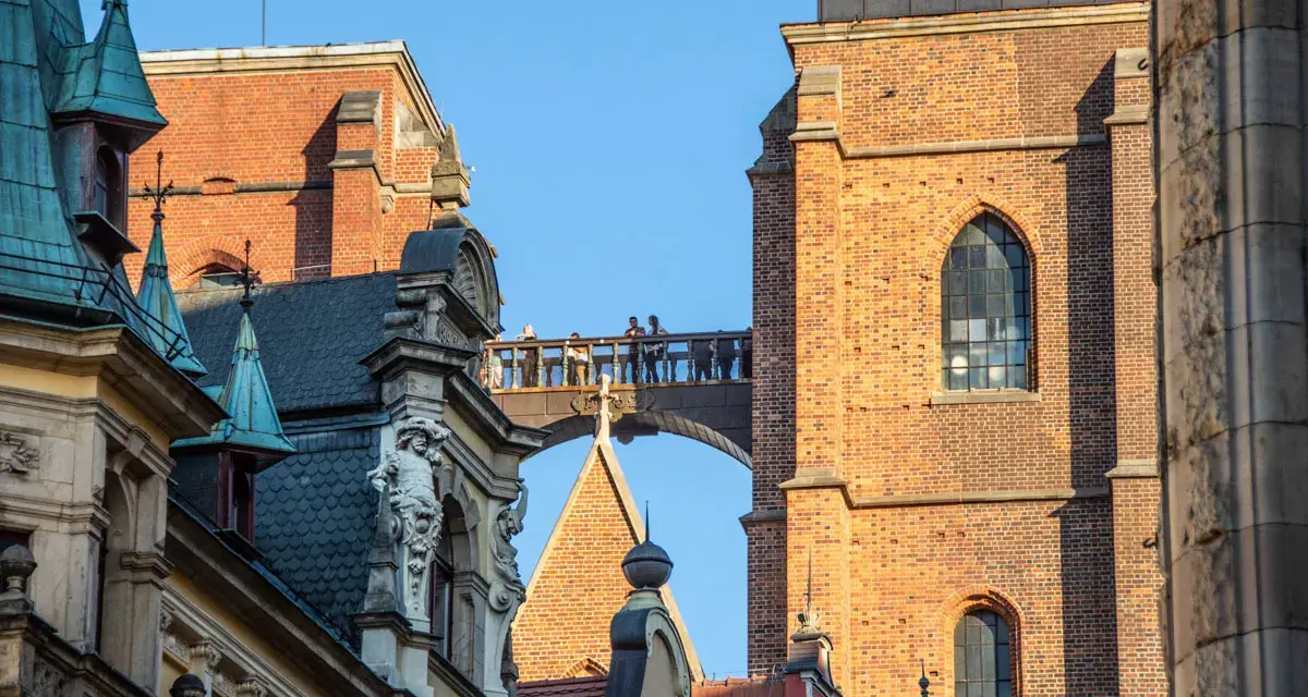 Most zabytkowych budynków we Wrocławiu z ludźmi na moście i wieżą Katedry w tle.