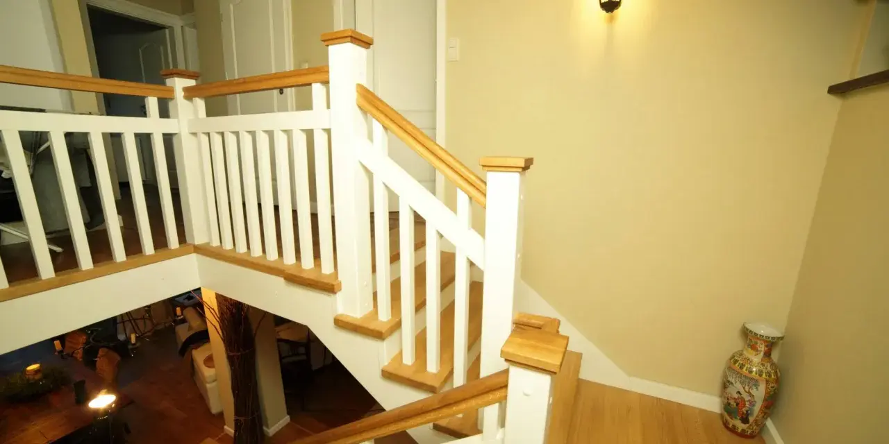 Elegancka klatka schodowa w stylu angielskim z białymi balustradami i drewnianymi elementami.