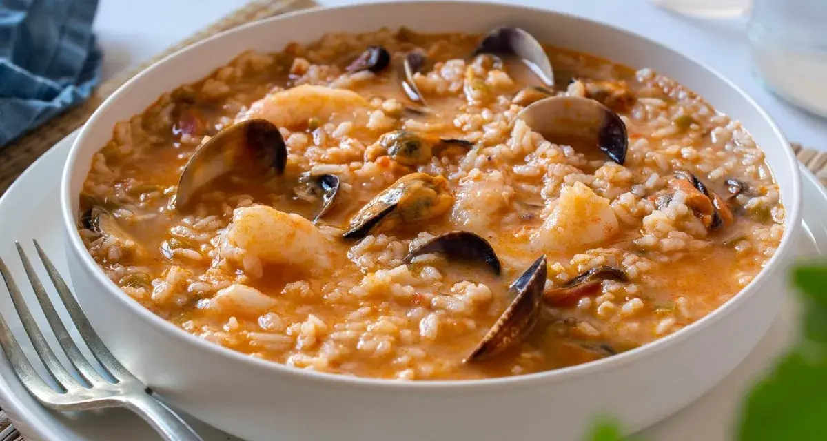 Un delicioso arroz caldoso de marisco, repleto de gambas, mejillones y almejas, servido en un cuenco blanco.