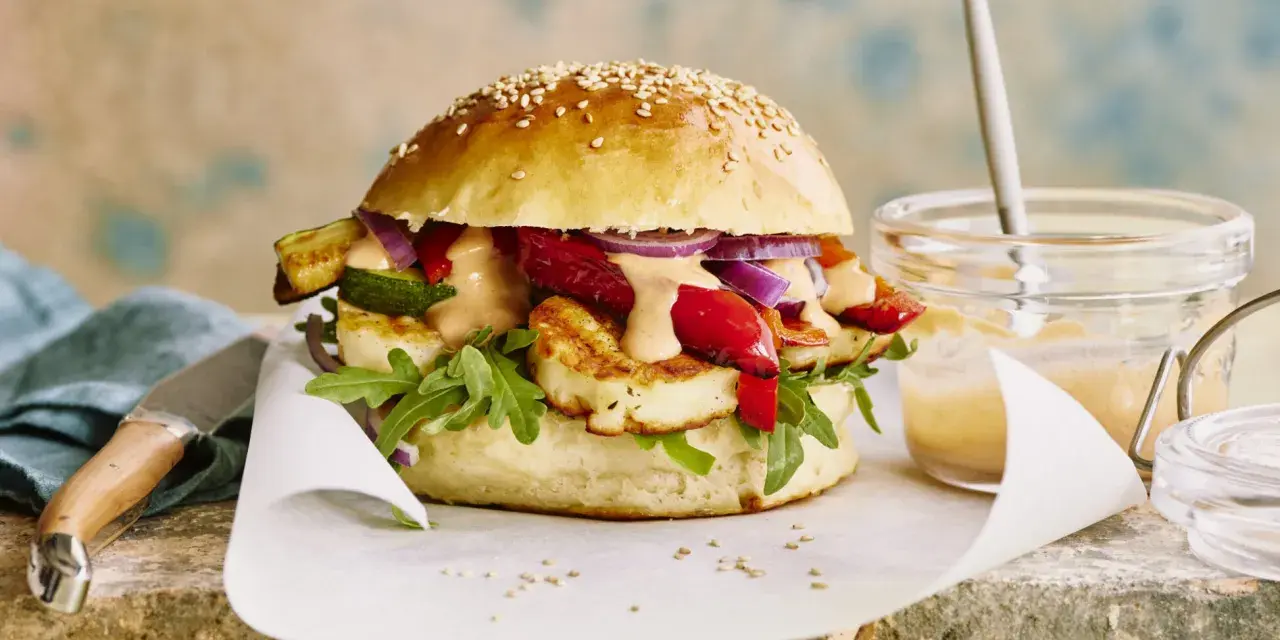 Saftiger halloumi burger mit gegrilltem Gemüse, Rucola und cremiger Sauce auf einem Sesambrötchen.