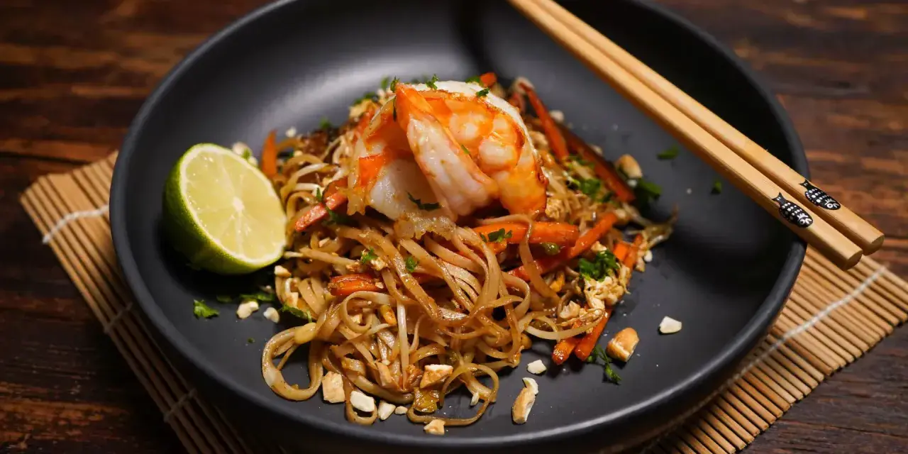Ein Teller Pad Thai mit Garnelen, Limette und Erdnüssen, bereit zum Genießen.