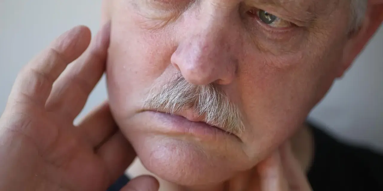 Mann mit Schnurrbart, der sich mit den Fingern das Gesicht berührt, als ob er ein Kribbeln im Gesicht spürt.