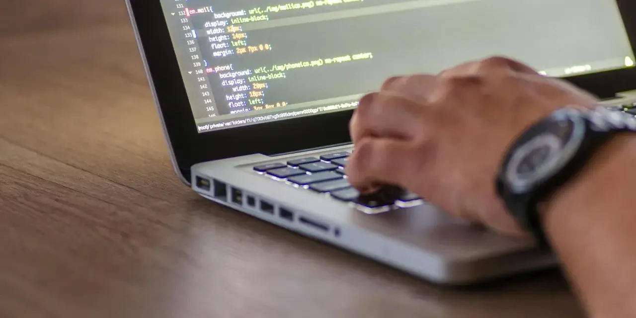 Kodowanie strony internetowej, widać fragment kodu HTML z listą nieuporządkowaną i rękę piszącą na klawiaturze.