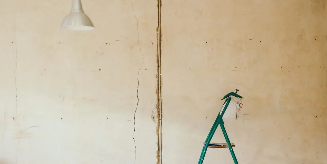 Pękające ściany starego domu, widoczna instalacja elektryczna i drabina.