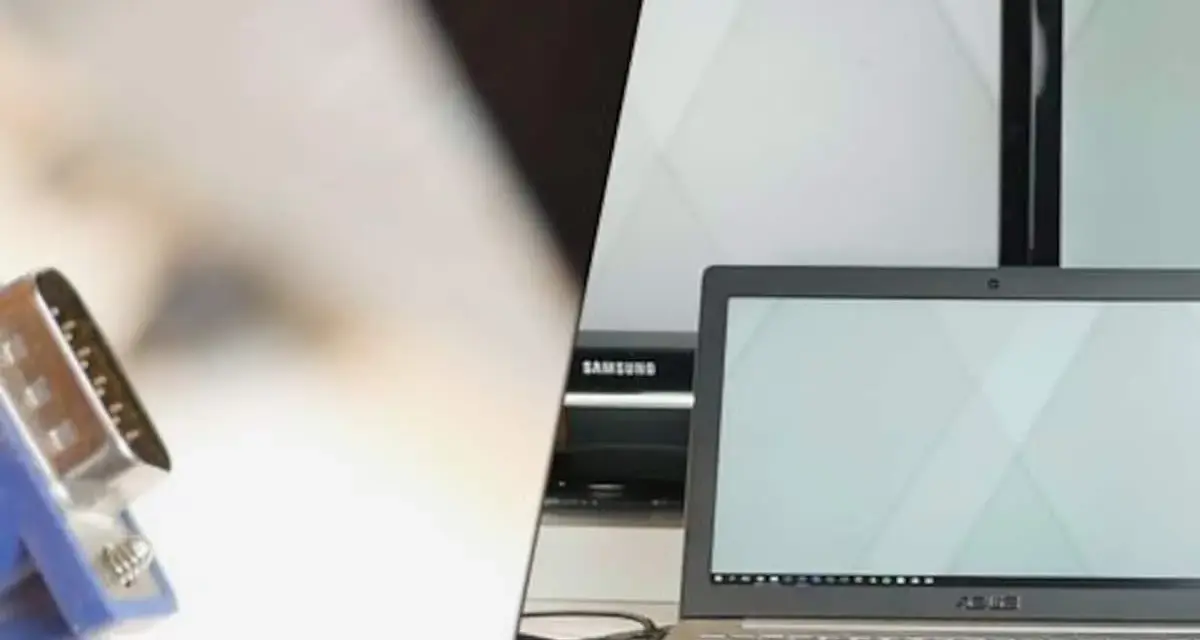 Ein VGA-Kabel wird verwendet, um einen Laptop mit einem Bildschirm zu verbinden. Mehrere Monitore sind im Hintergrund zu sehen.
