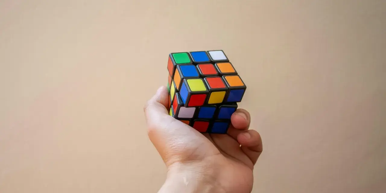 En hand håller en färgglad rubiks kub nyckelring mot en ljus bakgrund.