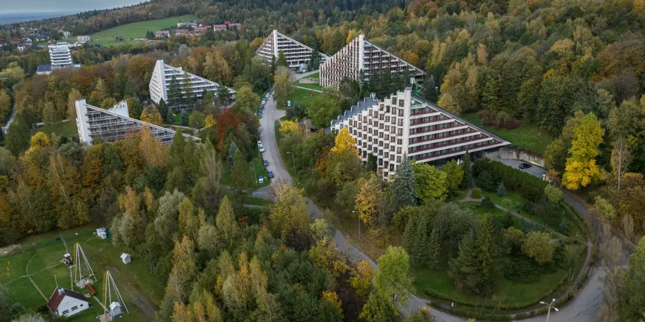 Widok z lotu ptaka na sanatoria o trójkątnej architekturze w otoczeniu jesiennego lasu.