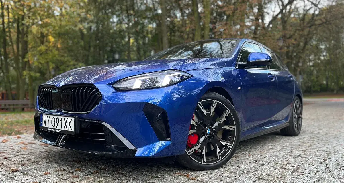 Błękitne, sportowe niemieckie auto BMW z czarnymi felgami i czerwonymi zaciskami hamulcowymi stoi na brukowanej drodze wśród jesiennych drzew.