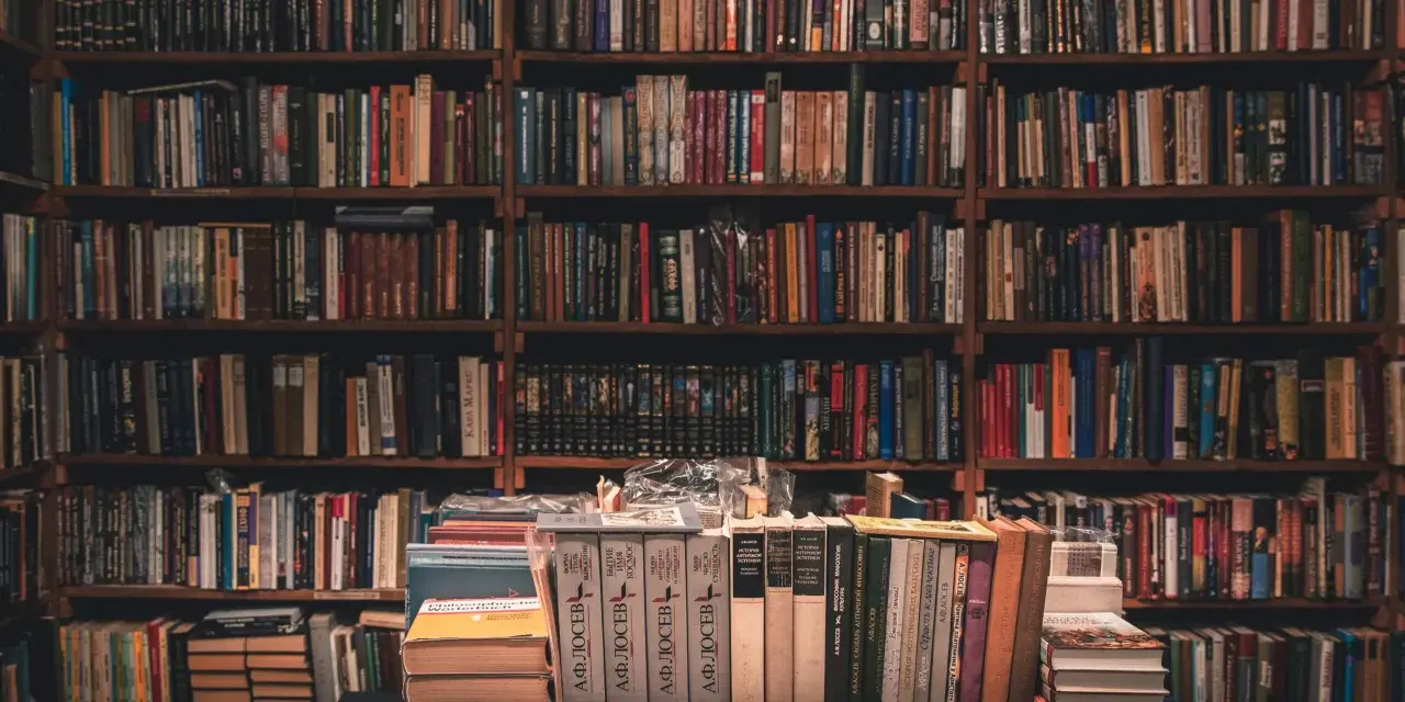 Wielka biblioteka pełna książek. Na pierwszym planie stosy książek, jedna z nich przypomina bułeczkę.