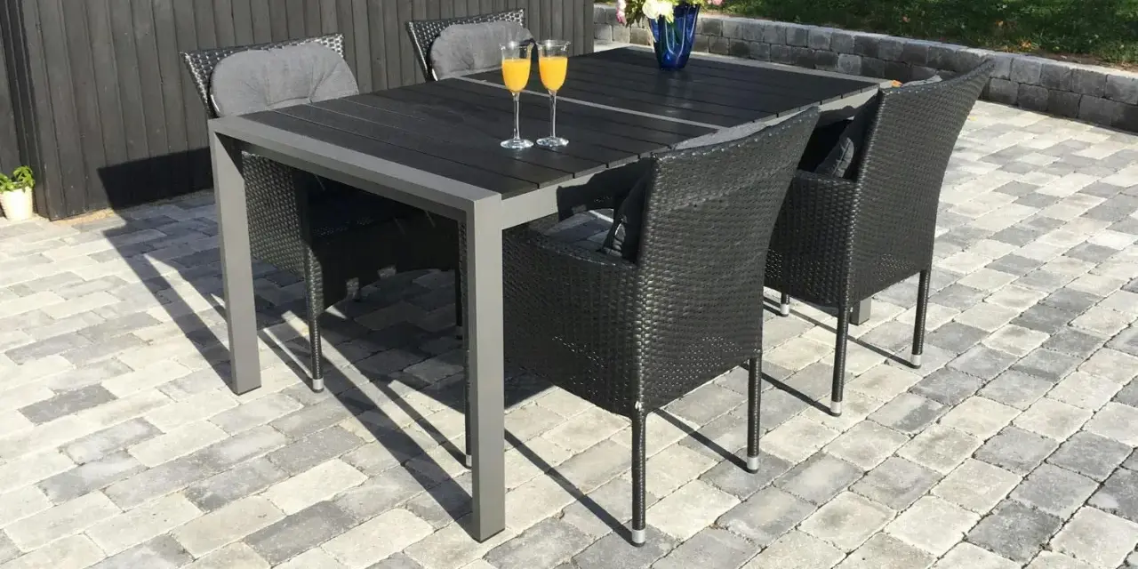 En uteplats med stenläggning, ett mörkt bord med korgstolar och glas med juice.