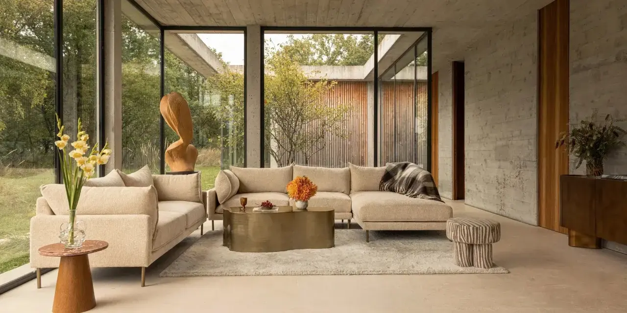 Sofá seccional beige y sillón en un salón moderno con grandes ventanales. Las combinaciones con beige crean un ambiente sereno y elegante.