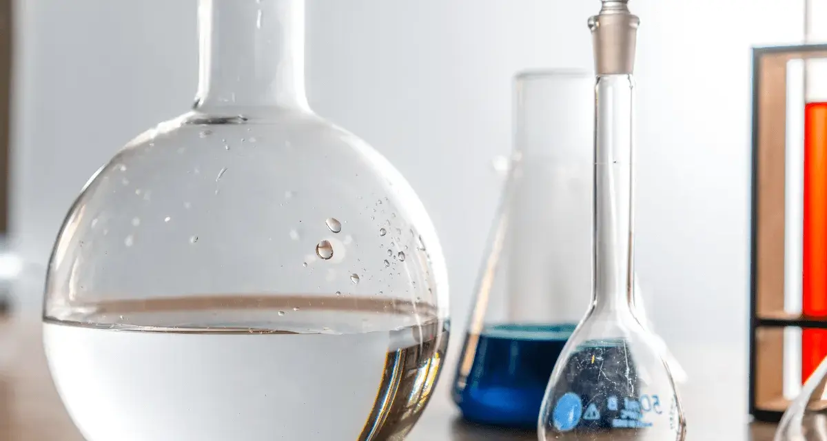 Laboratorieglas med vatten och blå vätska. Frågan om man kan dricka destillerat vatten är relevant i vetenskapliga sammanhang.