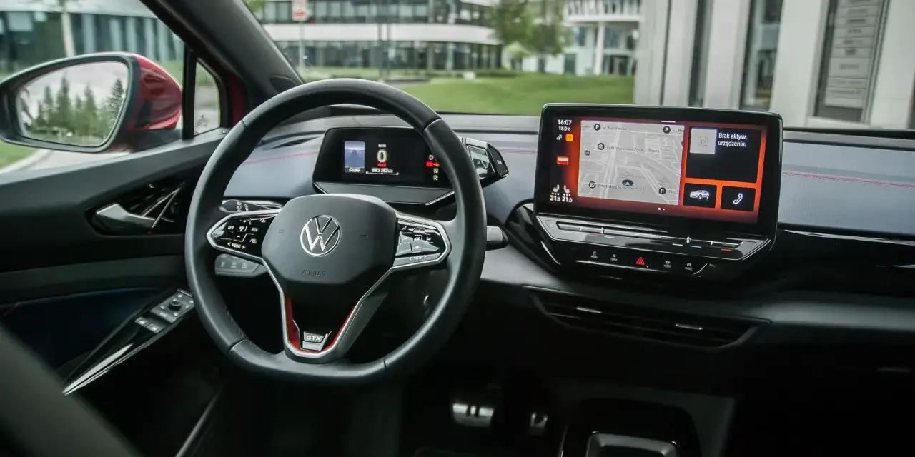 Wnętrze Volkswagena ID.4 GTX z ekranem nawigacji i cyfrowym kokpitem. Kierownica z przyciskami i oznaczeniem GTX.
