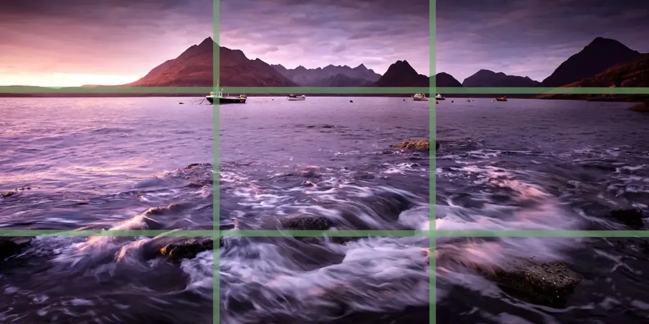 Paysage marin au crépuscule, avec des montagnes en arrière-plan et des bateaux sur l'eau. La composition suit la règle des tiers pour un équilibre visuel.