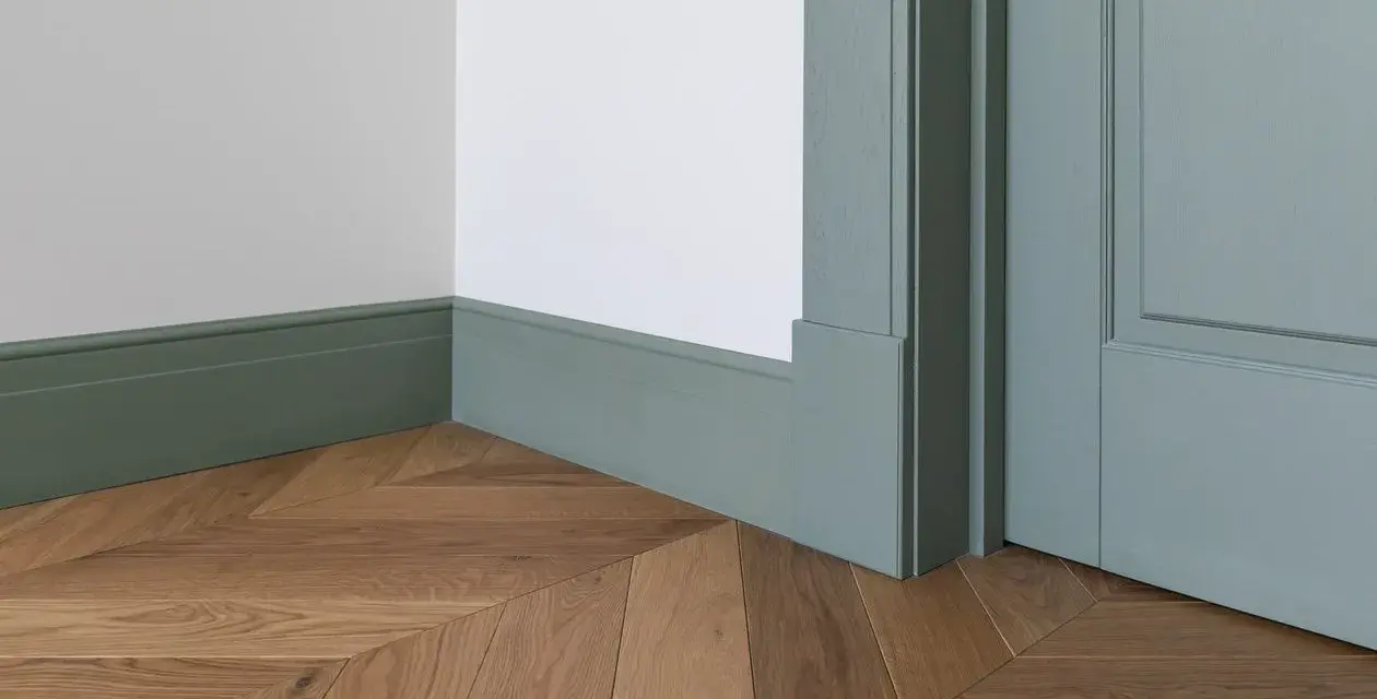 Elegancka listwa przypodłogowa w kolorze miętowym, z widocznymi wymiarami, idealnie komponuje się z drewnianą podłogą ułożoną we wzór jodełki.