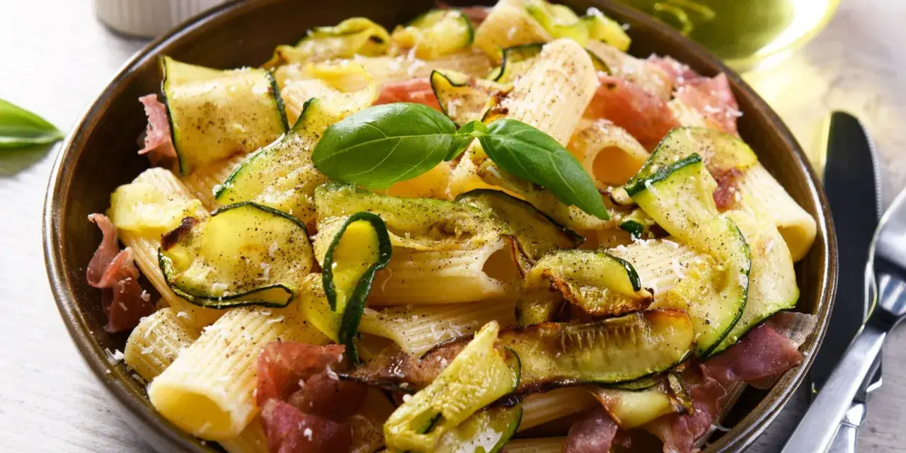 Proste danie włoskie: makaron rigatoni z cukinią, szynką parmeńską i bazylią.