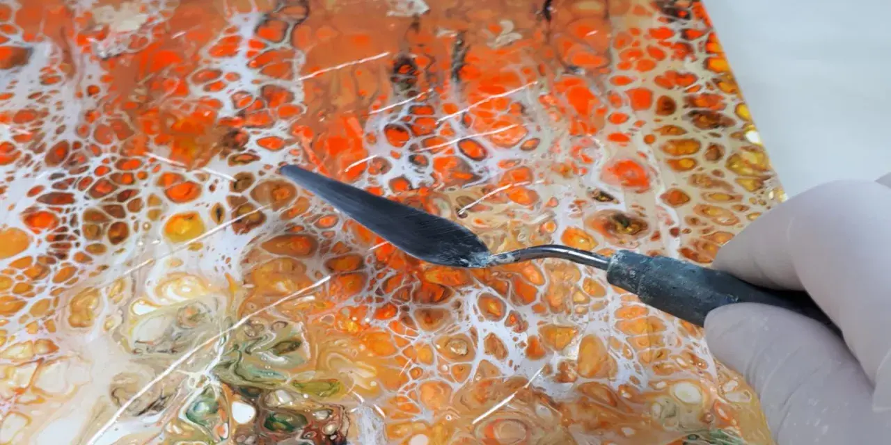 Maintenant, peut-on mettre de la résine sur de la peinture acrylique ? Un outil est utilisé pour travailler une peinture abstraite aux couleurs vives, orange et blanc.