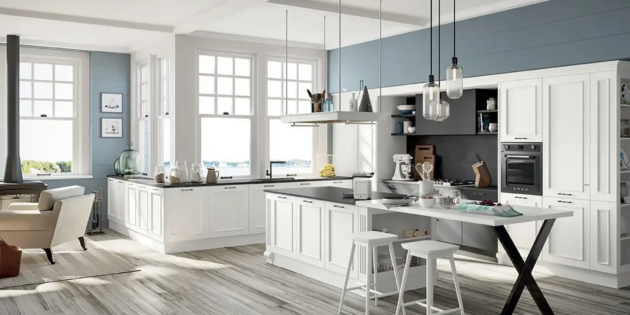 Cucina luminosa con isola centrale, sgabelli bianchi e una nicchia sotto finestra con vista mare.