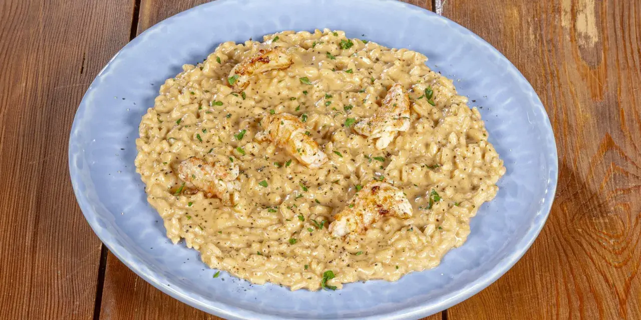 Un cremoso risotto alla crema di scampi, guarnito con scampi scottati e prezzemolo tritato, servito su un piatto azzurro.