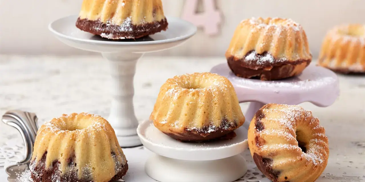 Mehrere mini Gugelhupf mit Puderzucker bestäubt, auf verschiedenen Etageren arrangiert.