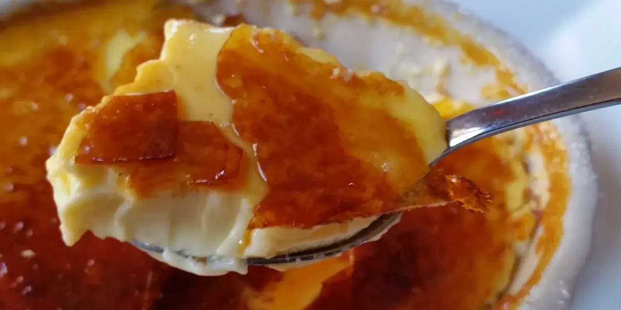 En sked tar en bit av en krämig creme brulee med karamelliserat socker. Perfekt dryck till creme brulee.