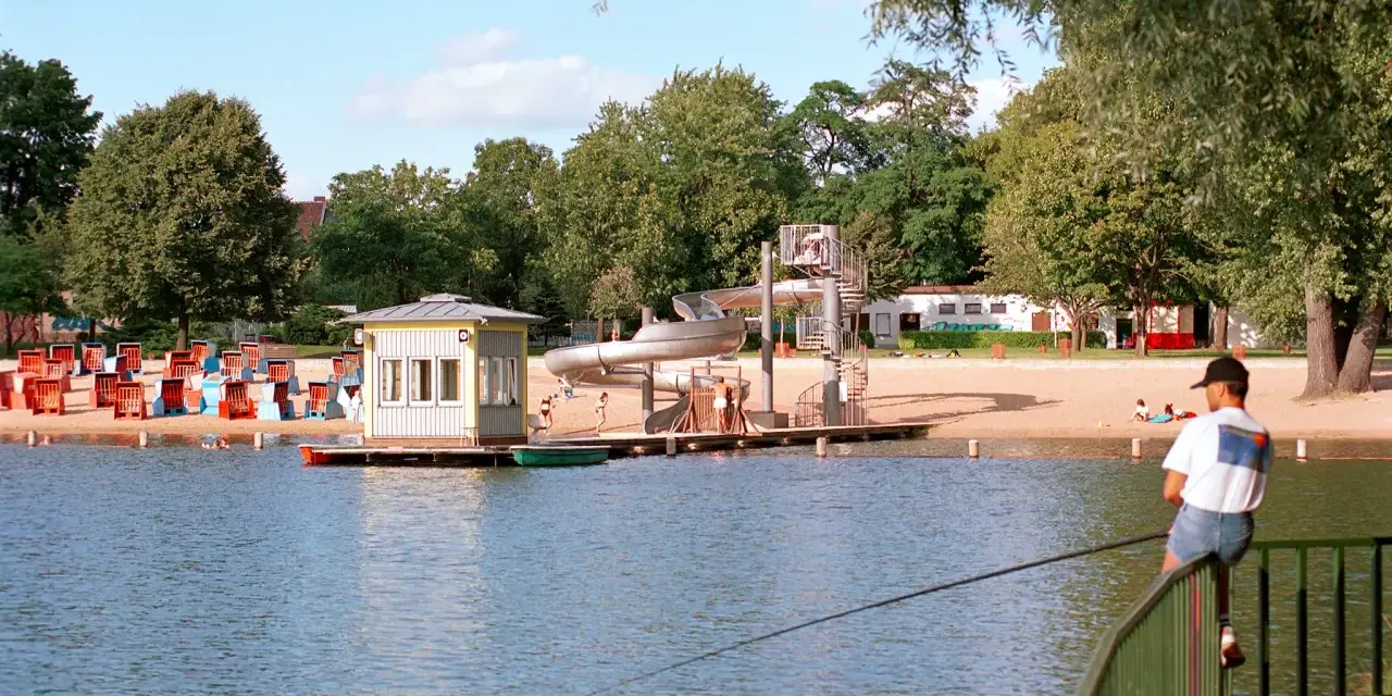 Am Orankesee Strandbad tummeln sich Badegäste, während ein Angler geduldig auf seinen Fang wartet.