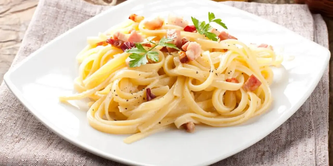 Pyszne Spaghetti Carbonara przepis na talerzu, udekorowane natką pietruszki i kawałkami boczku.